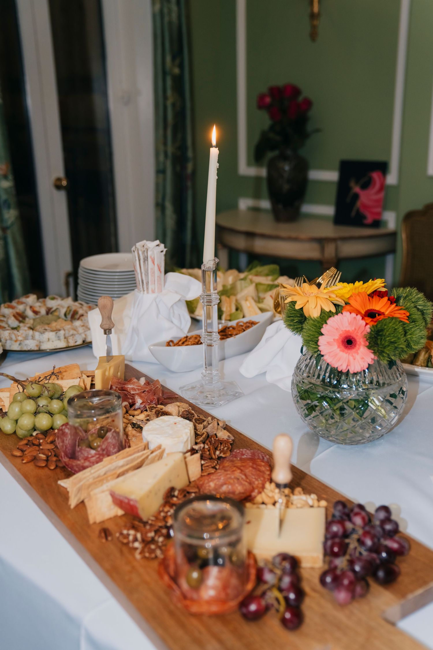 Elegant charcuterie board spread with cheeses, meats, fruits and nuts illuminated by glowing candles at an upscale event.
