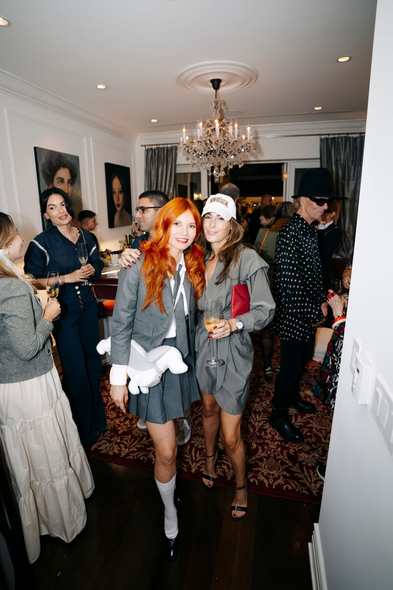 Indoor party scene with chandelier lighting and patterned carpet showing guests mingling in casual attire.