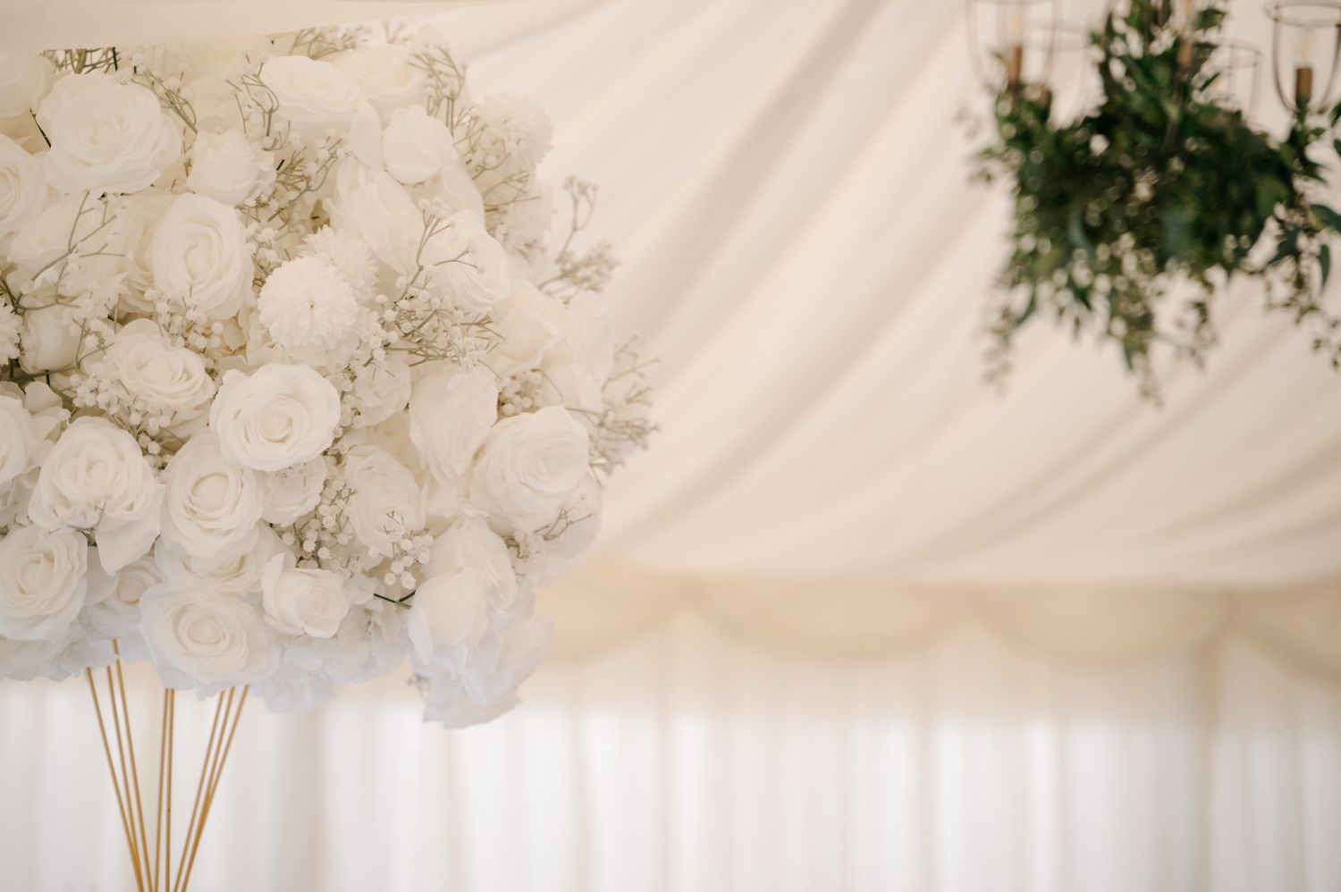 White floral wedding decorations with roses and greenery against draped fabric backdrop.