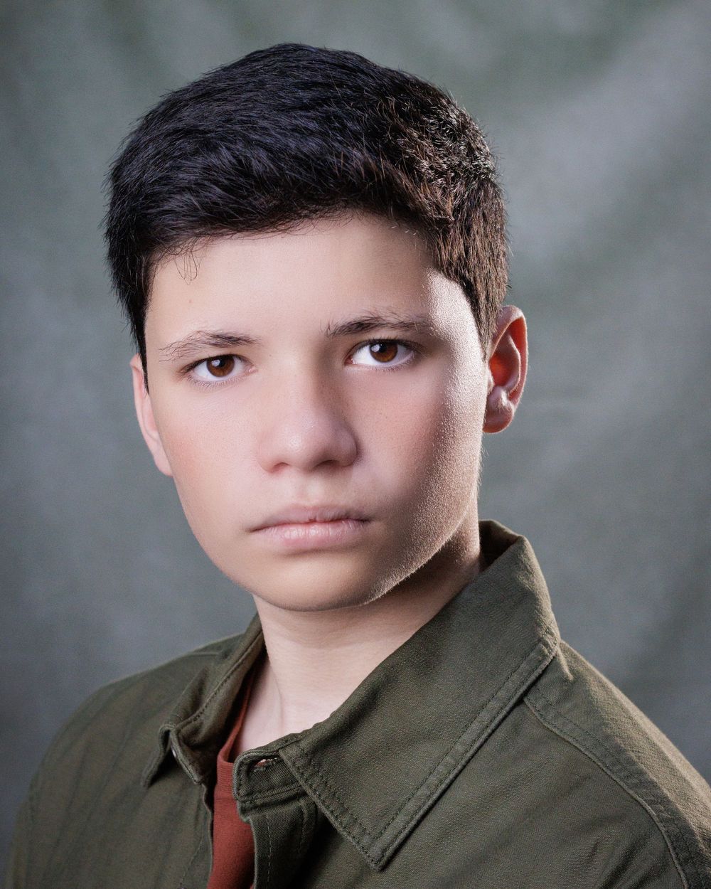 A portrait photograph of a young person in an olive green jacket against a soft blurred background.
