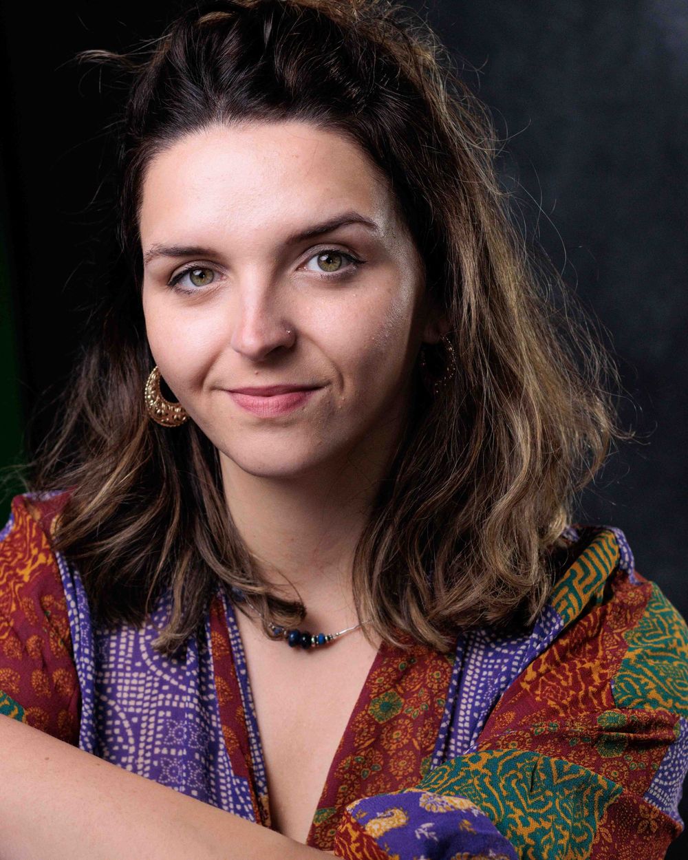 A person in a colorful patterned top with purple and orange details poses against a dark background in a portrait series.