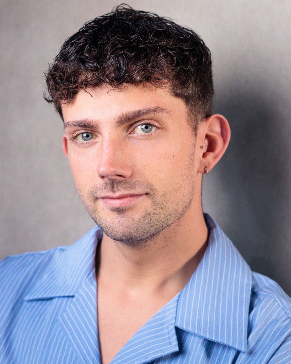 Professional headshot portrait with blue striped button-down shirt against a light gray studio background.