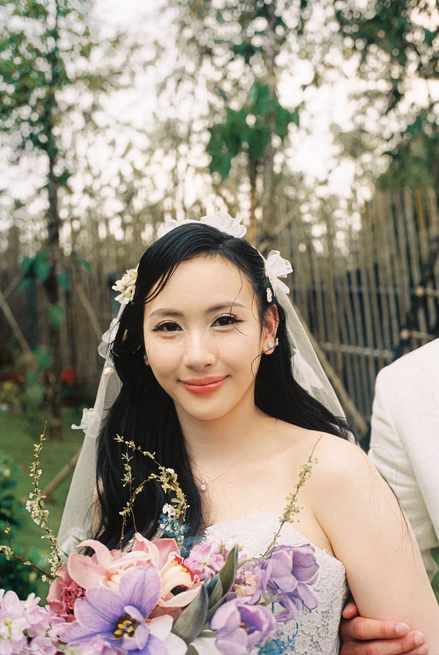 Joyful bride wearing a white floral headpiece and veil smiles while holding colorful flowers.