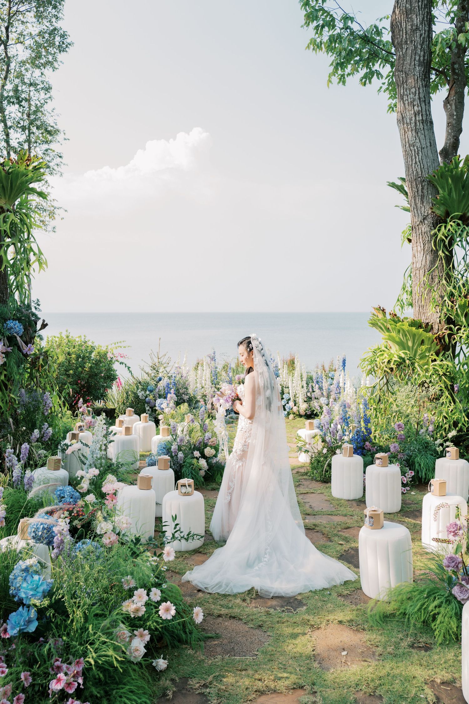 Garden wedding ceremony setup with white lanterns, hydrangeas, and ocean view backdrop.