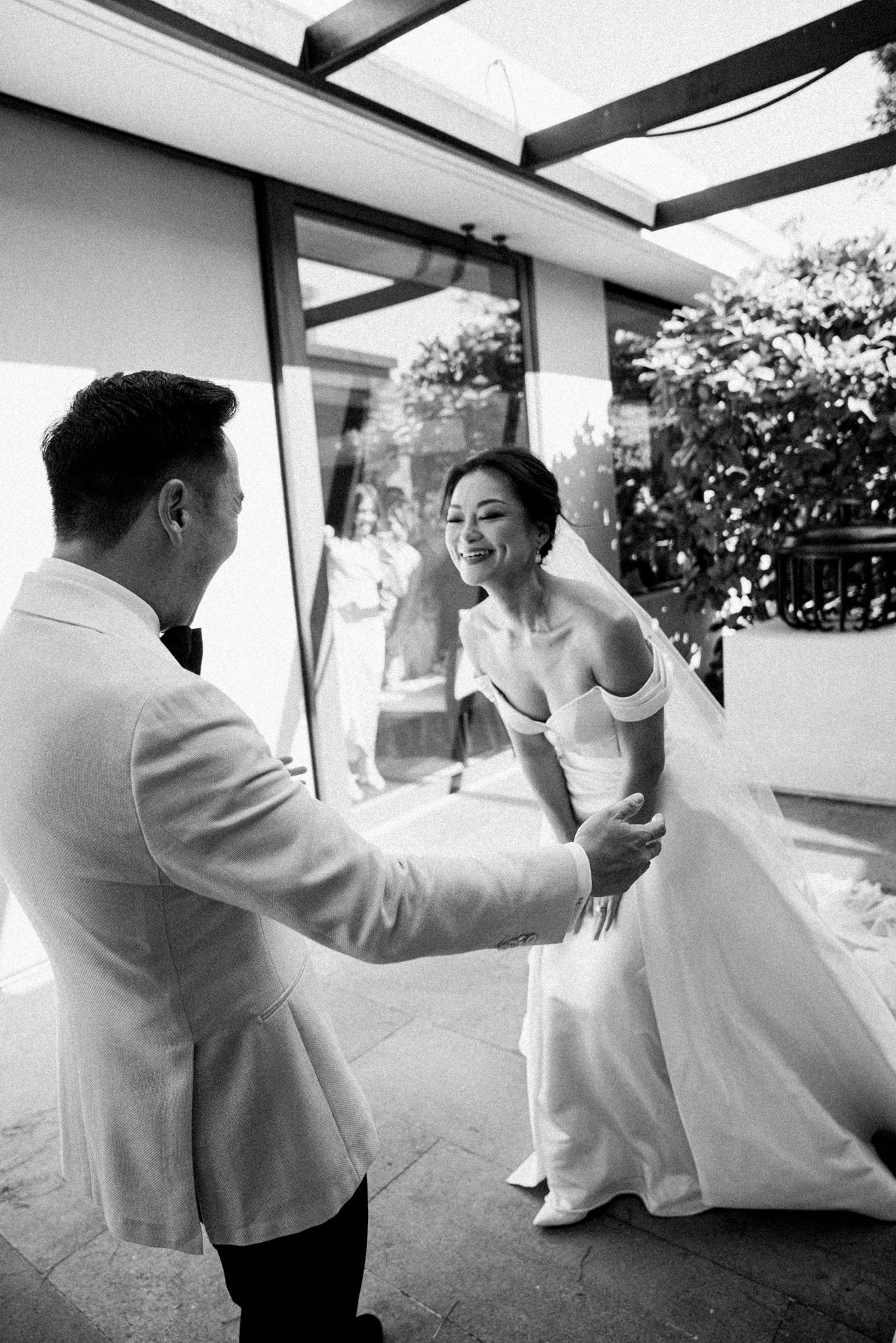 Candid black and white moment between a couple in wedding attire on a sunlit patio.