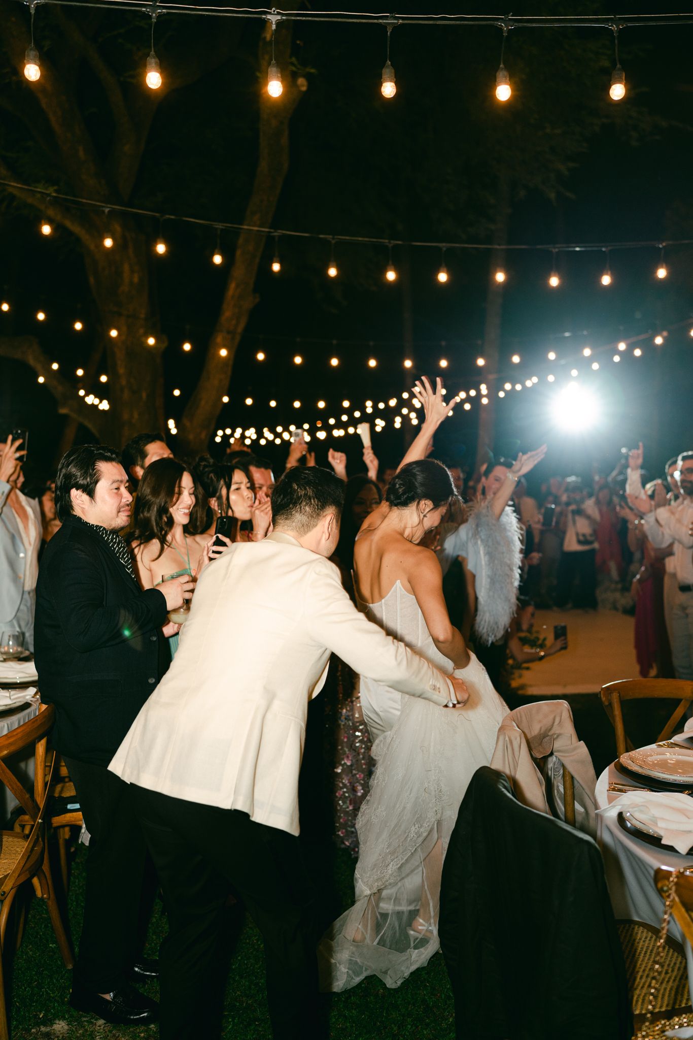 Outdoor wedding reception with string lights and dancing guests under the night sky.