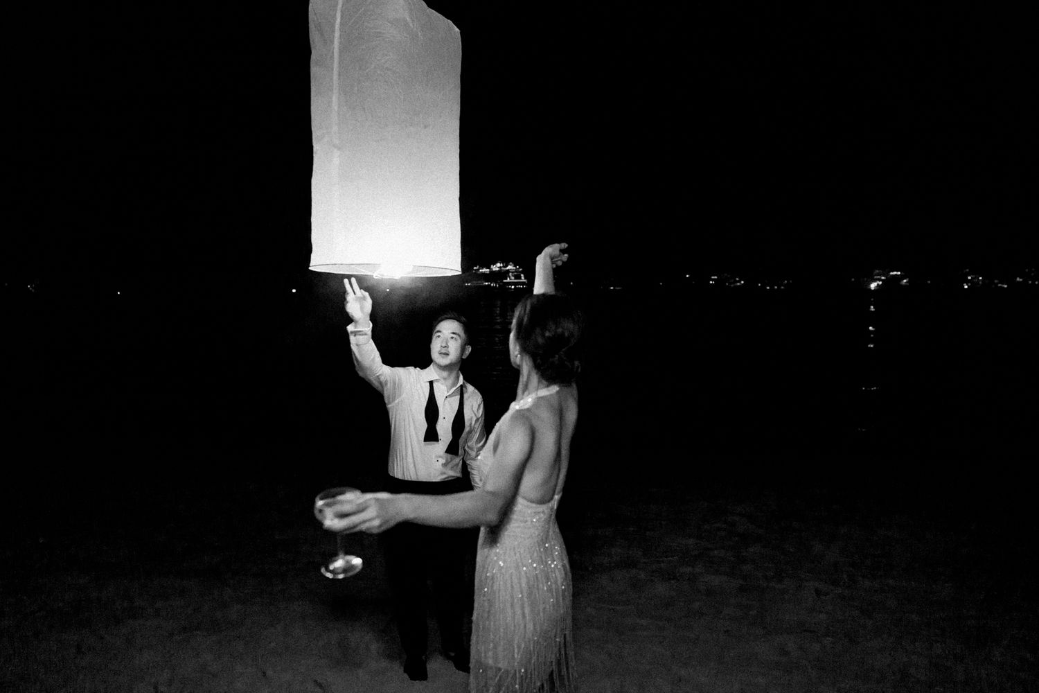 Two people releasing a glowing paper lantern into the dark night sky.