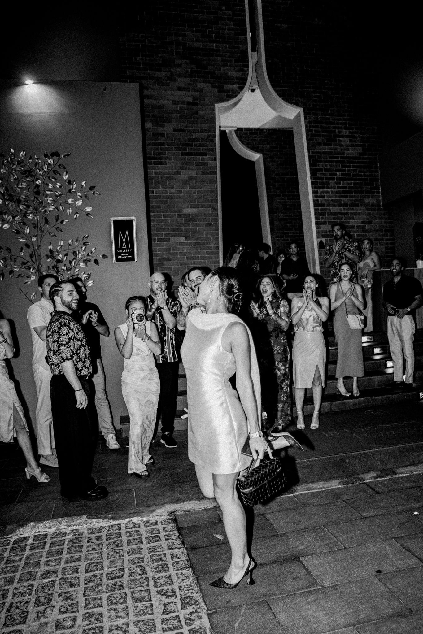 Black and white photo of wedding guests lined up outside a brick building at night.