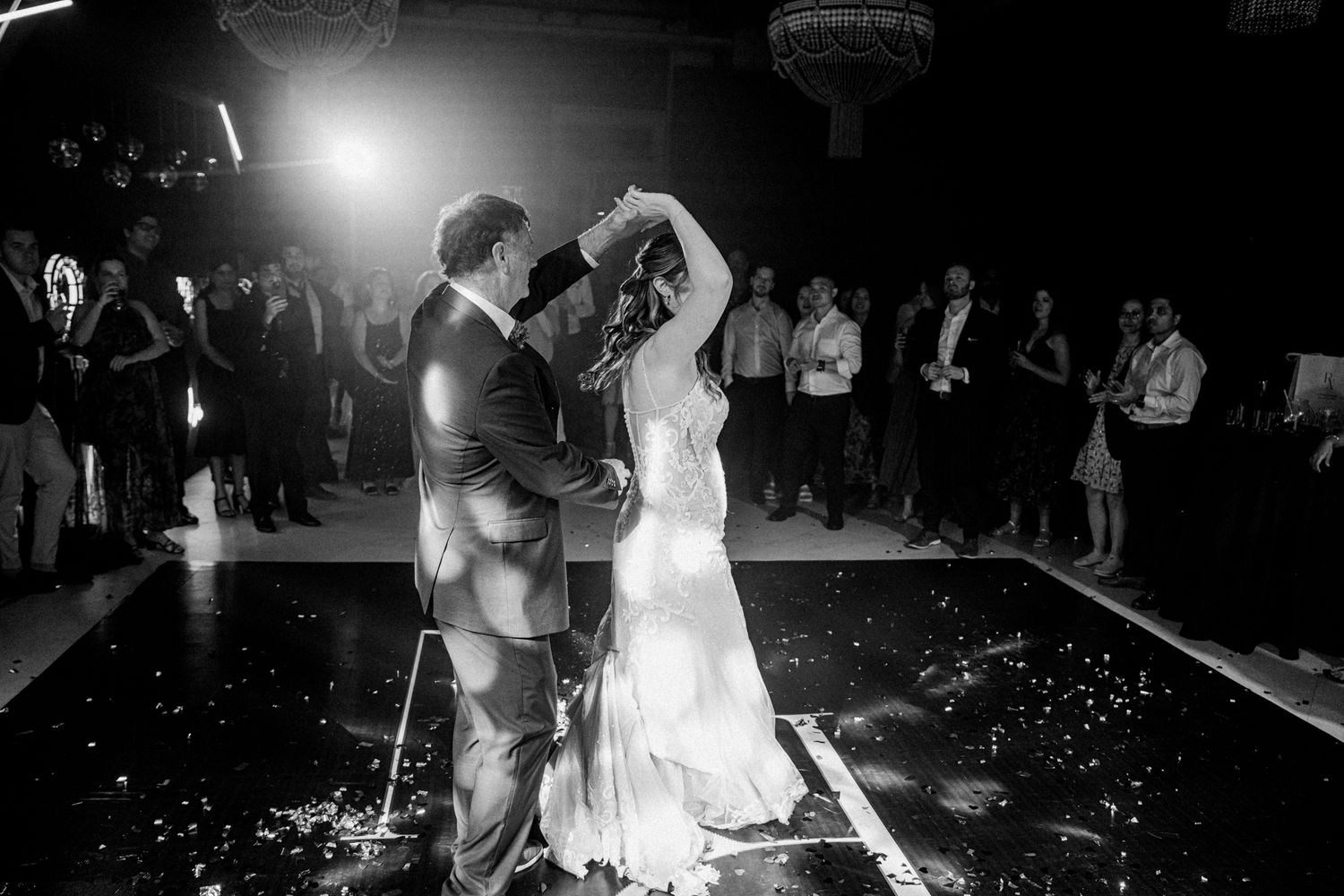 Couple shares their first dance as newlyweds under dramatic lighting on a reflective dance floor.