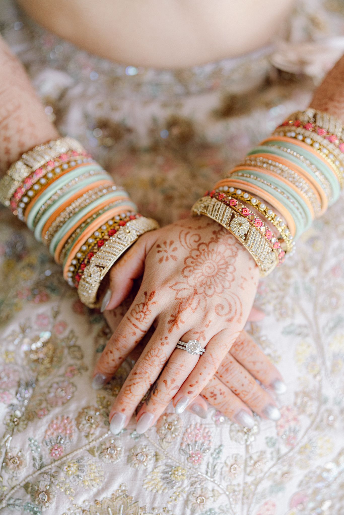 Close-up of traditional Indian bridal jewelry and henna adorned hands on embroidered fabric.