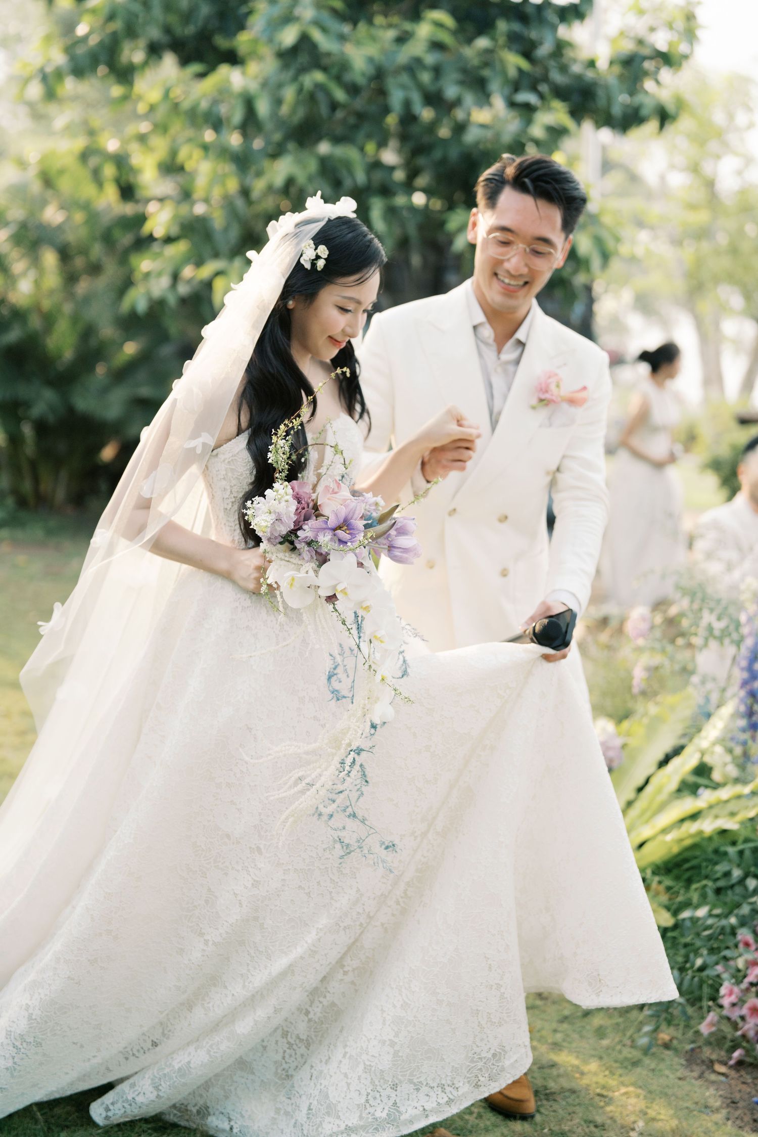 Romantic couple in elegant white wedding attire dancing together in a garden setting with natural sunlight.