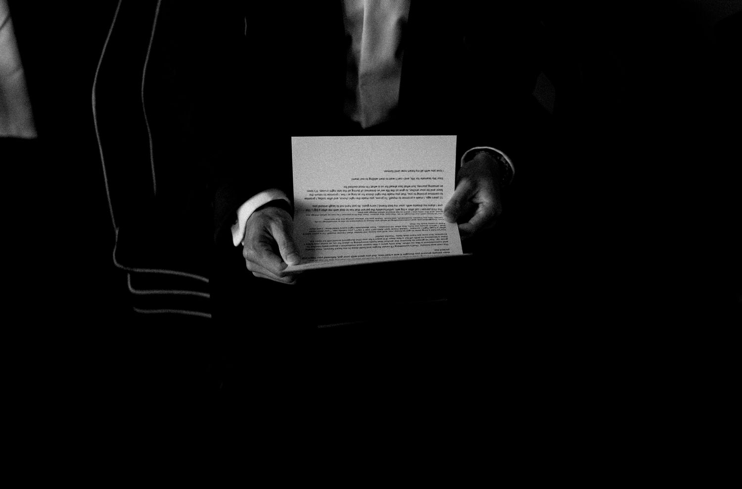 Hands holding a paper document in dramatic black and white lighting.