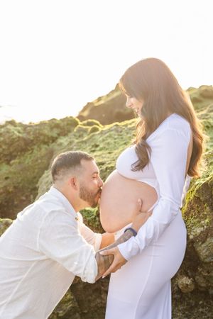 Romantic maternity photo session at sunset against rocky backdrop.