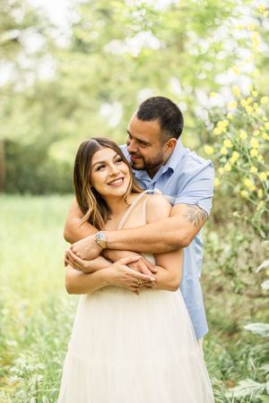 Romantic outdoor photoshoot with couple embracing in natural setting.