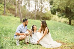 Family relaxing together on grassy hillside during outdoor photo session.
