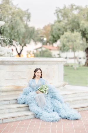 Person in flowing blue tulle dress posing elegantly on stone steps.