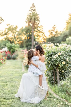 An intimate garden photoshoot with white dresses among flowering bushes at sunset.