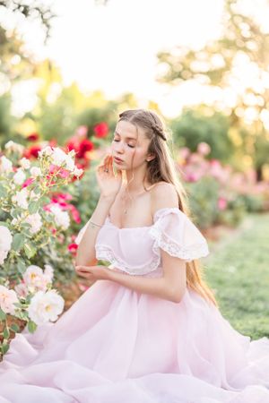 Woman in pink tulle dress poses elegantly in rose garden at golden hour.