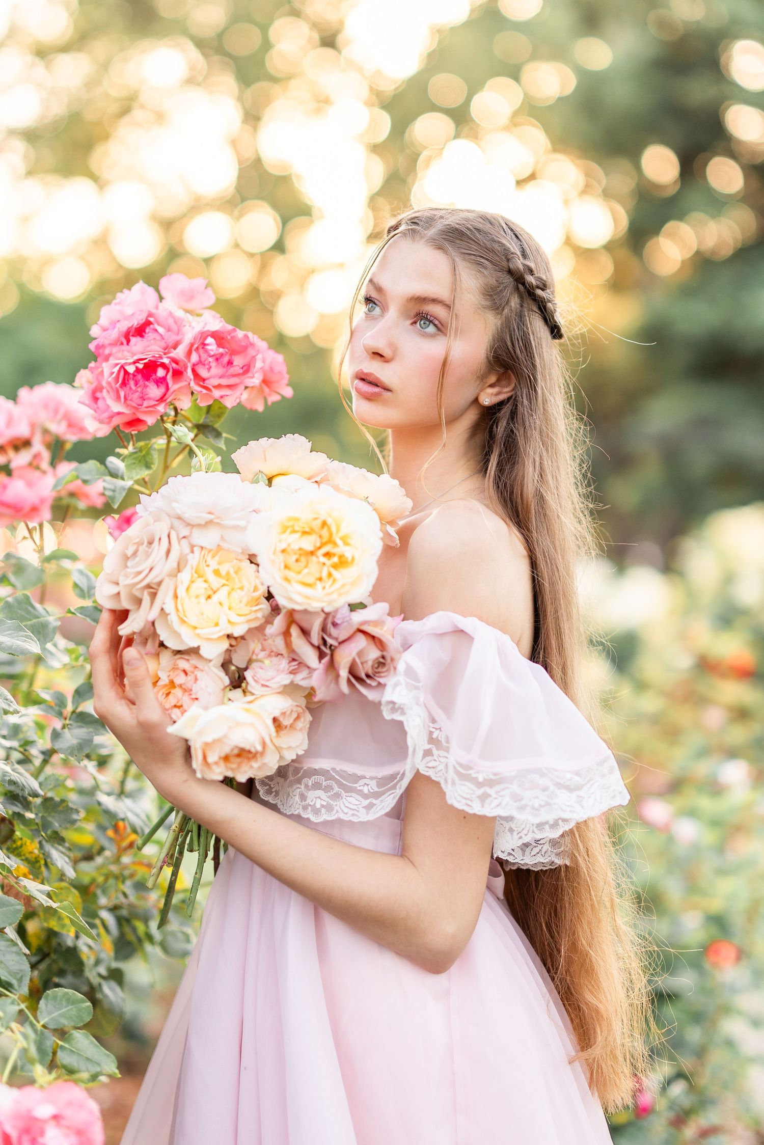 Woman in vintage pink dress poses with roses in a dreamy garden setting.