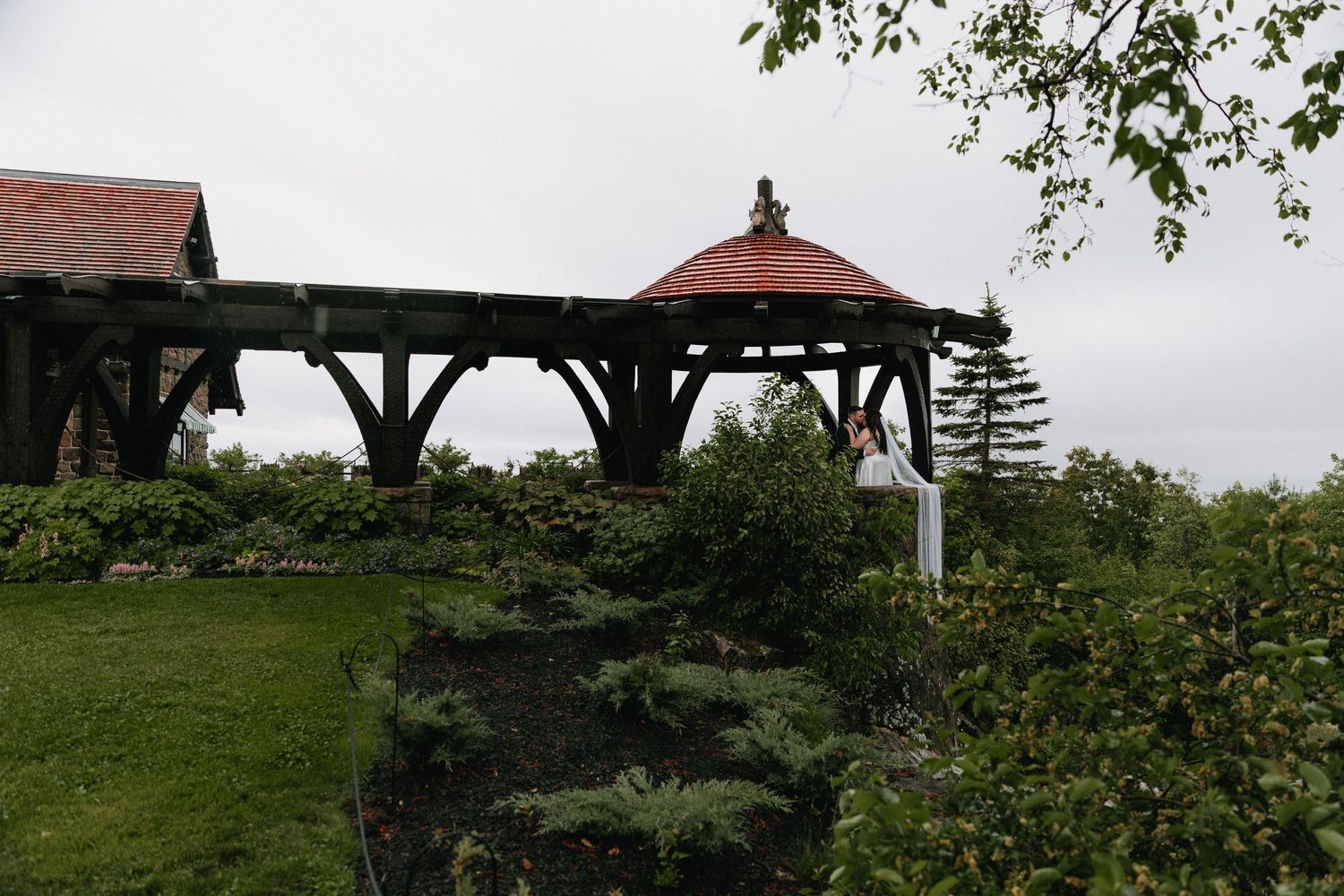 A wooden gazebo structure with red roof sits atop rocky terrain surrounded by greenery.