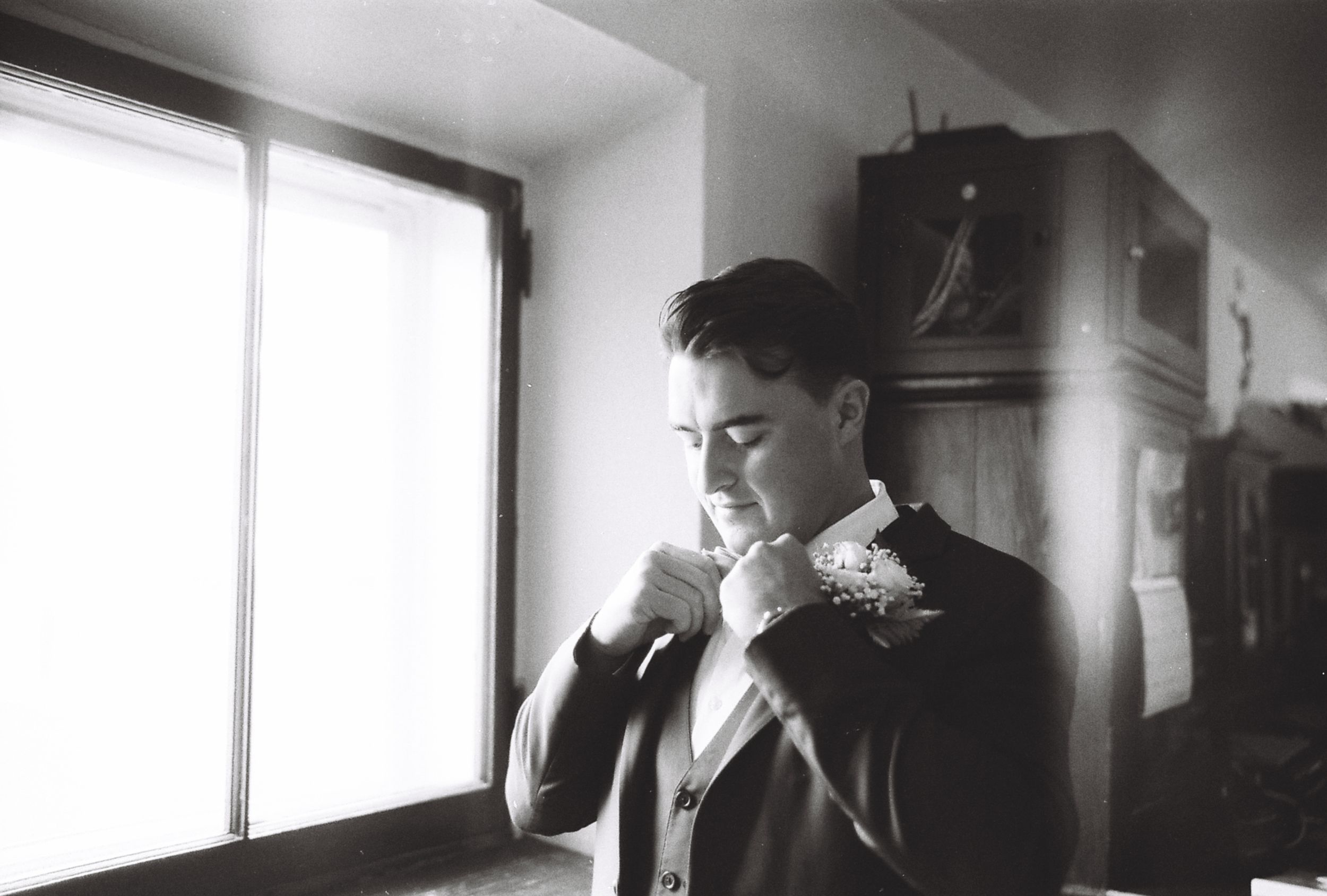 A vintage black and white photograph of someone adjusting their formal attire near a window.