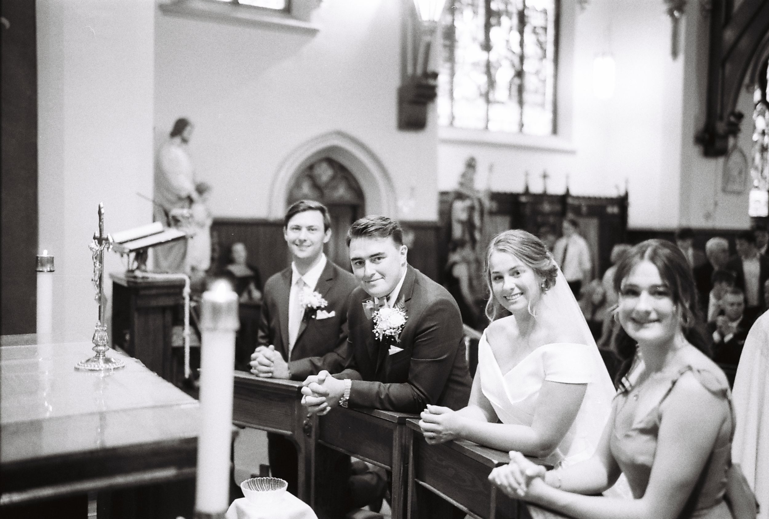 Wedding guests gathered inside an ornate church with stained glass windows and arched ceilings.