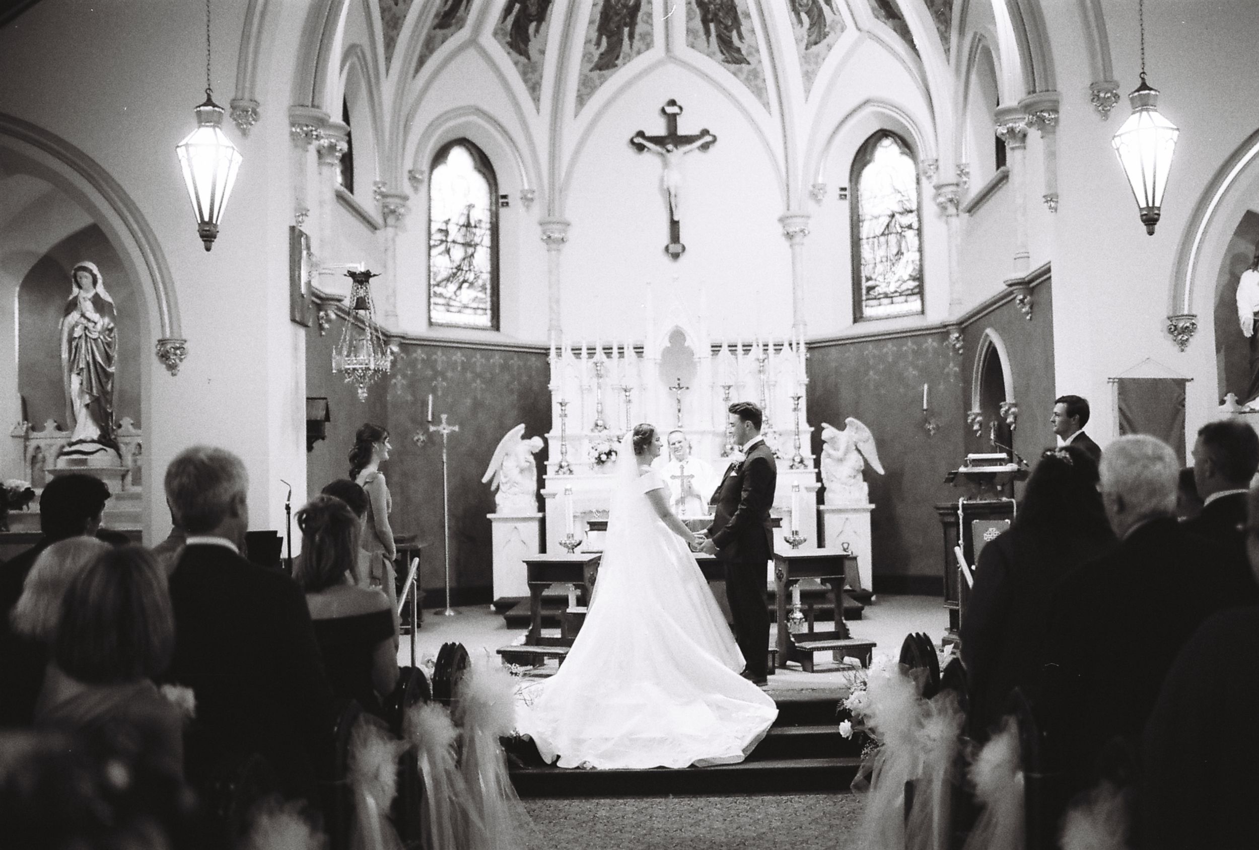 Wide angle panoramic view of a church wedding ceremony with guests seated in wooden pews.