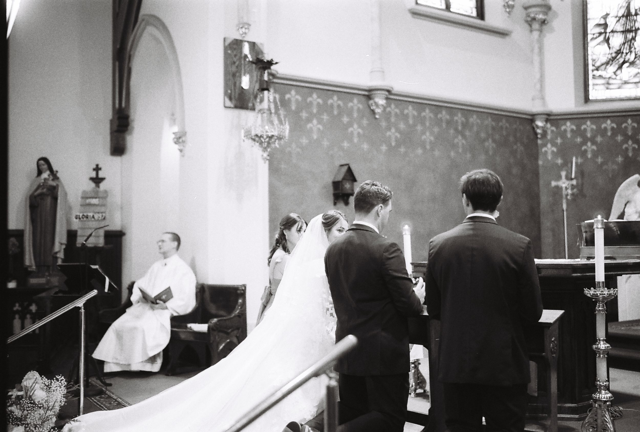 A black and white photograph of a wedding ceremony in progress at the altar of a traditional church.