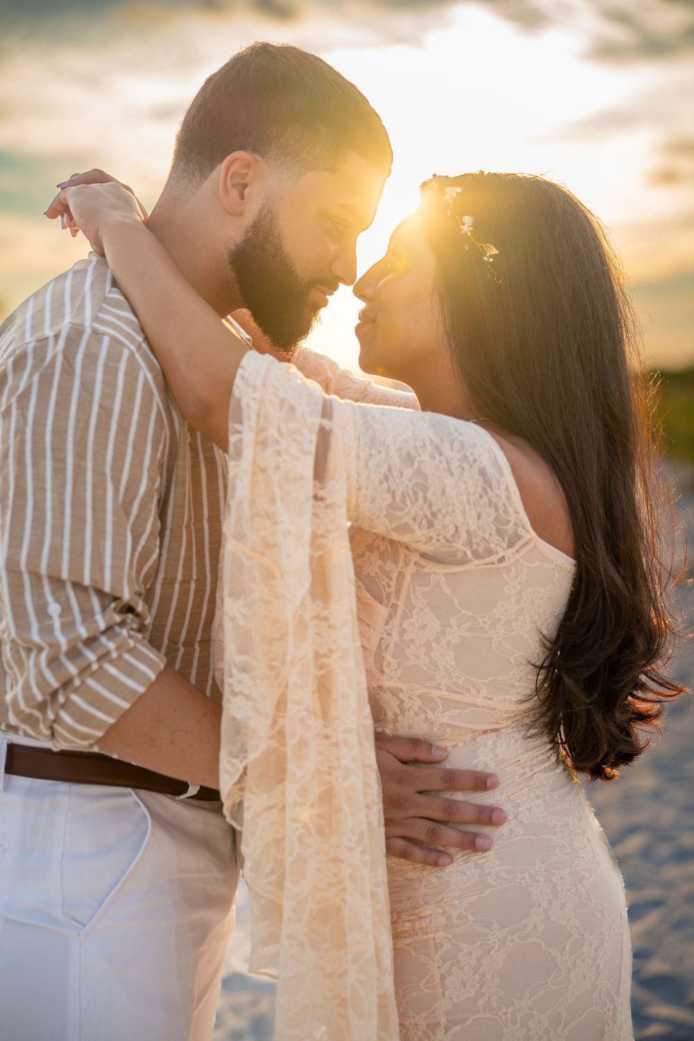 Romantic couple embraces during sunset beach photoshoot with dreamy golden light in background.