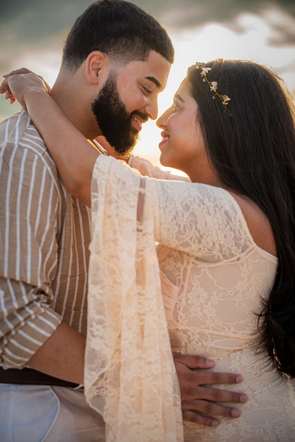 A romantic couple shares tender moments in a sunlit engagement photoshoot with a lace dress detail in focus.