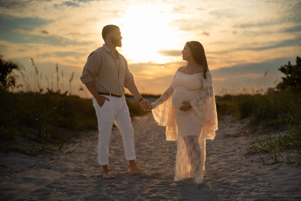 People in white outfits walking together on a sandy beach path at sunset, creating silhouettes against the golden sky.