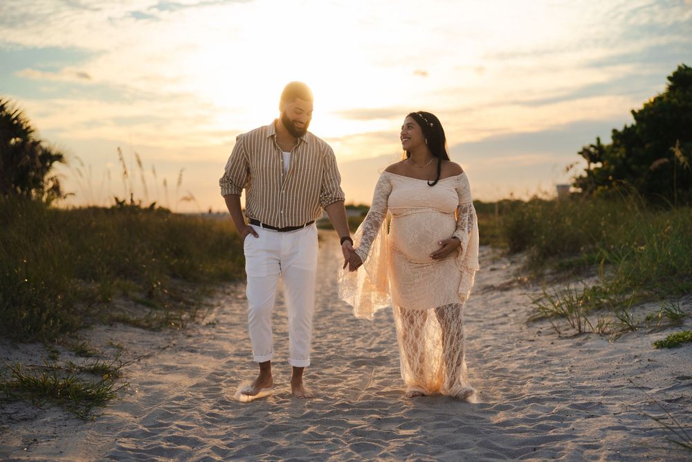 Couple walking together hand in hand on sandy beach path during golden sunset hour.