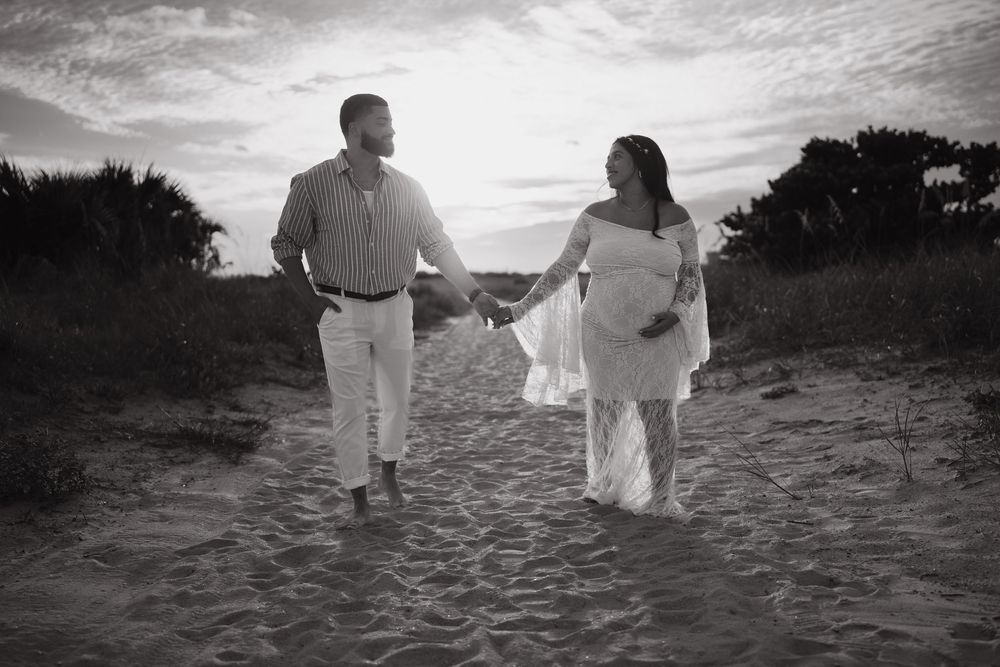 Couple in white outfits walking along a scenic beach during sunset creating romantic silhouettes.
