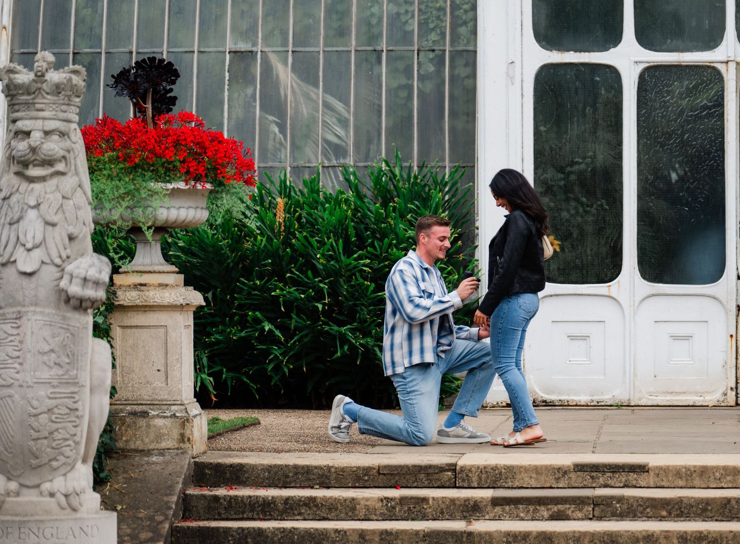 Students relax and study on stone steps outside a historic building with white-framed windows and red flowers.