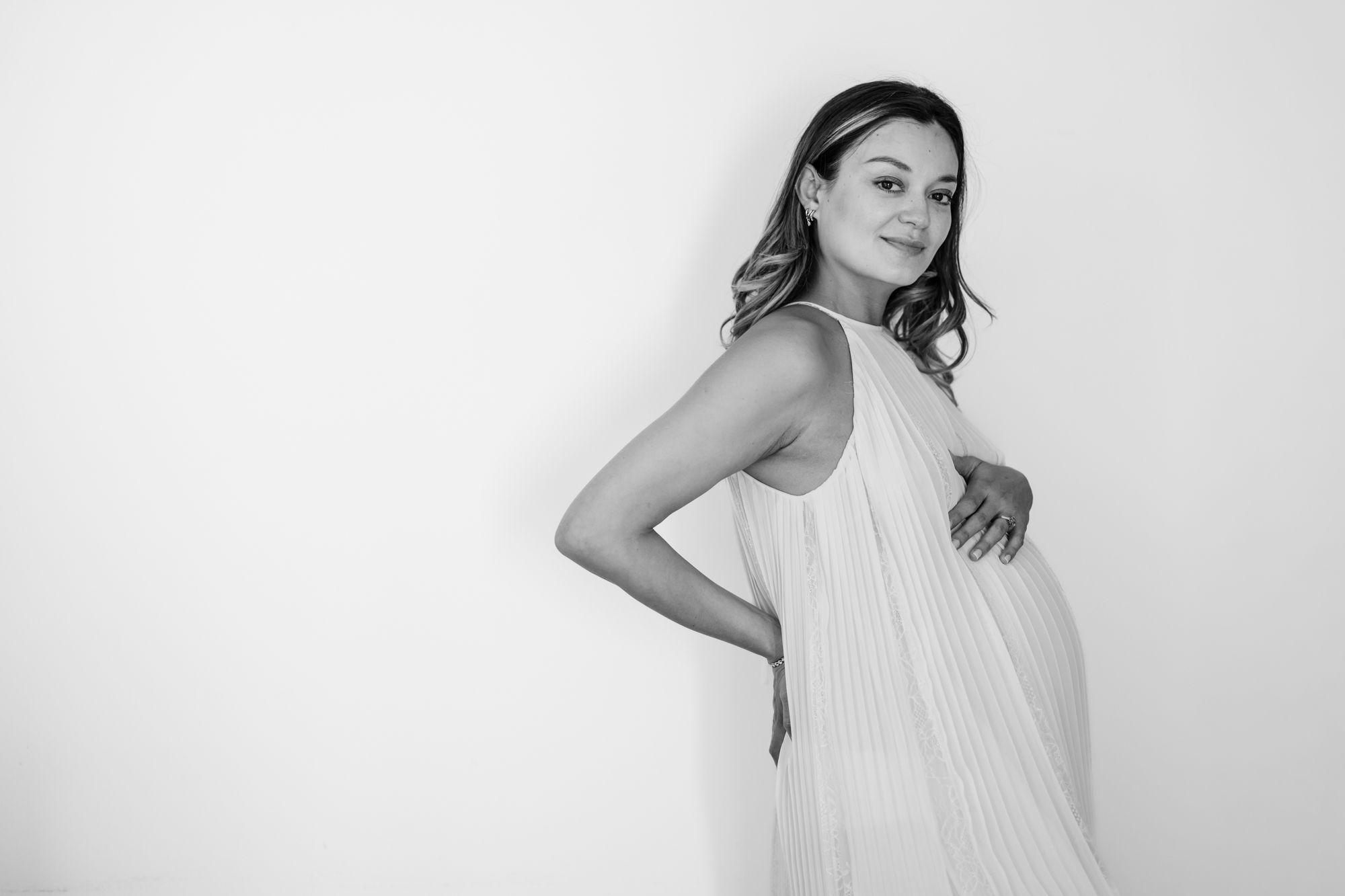 Woman in white sleeveless top poses against light background in minimalist fashion portrait series.