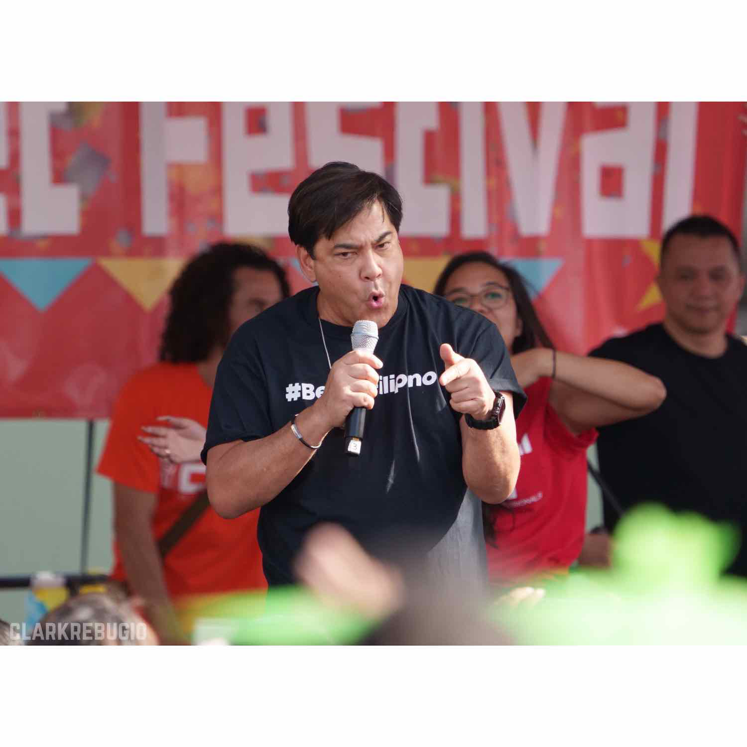 Man in a #BeingFilipino t-shirt addressing and engaging the audience at a Filipino cultural festival.