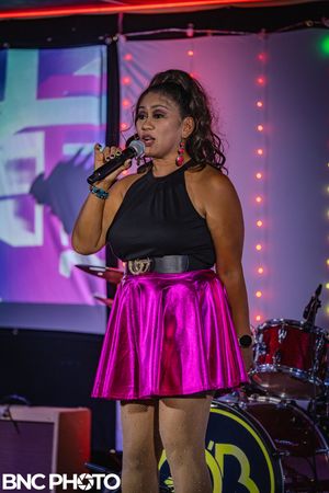 Female vocalist wearing a bright pink skirt performing under stage lights at a live concert.