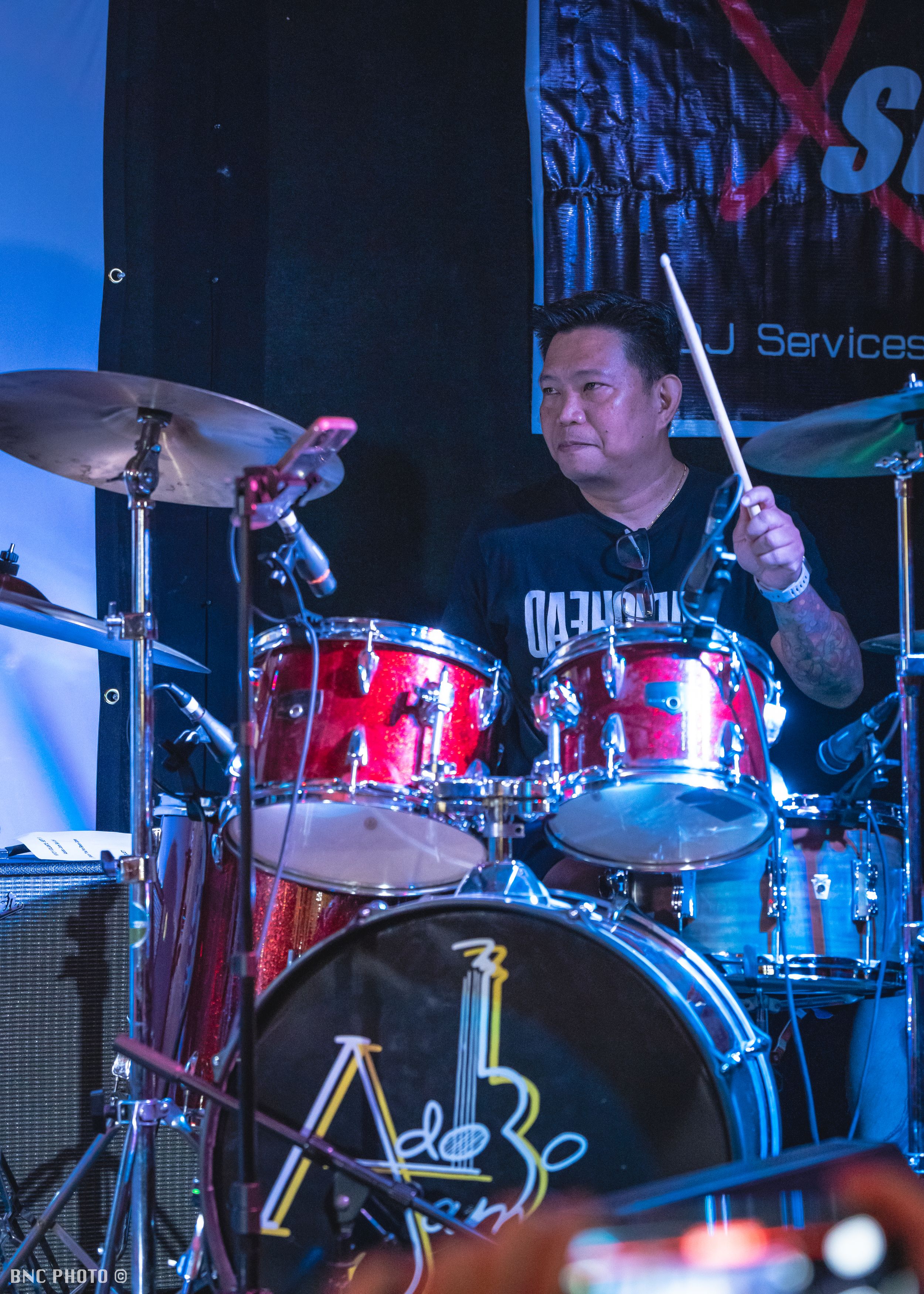 Male drummer playing a red drum kit during a live performance at a local music venue.
