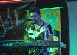 Male musician performing on keyboard on stage under green lighting at a local concert.