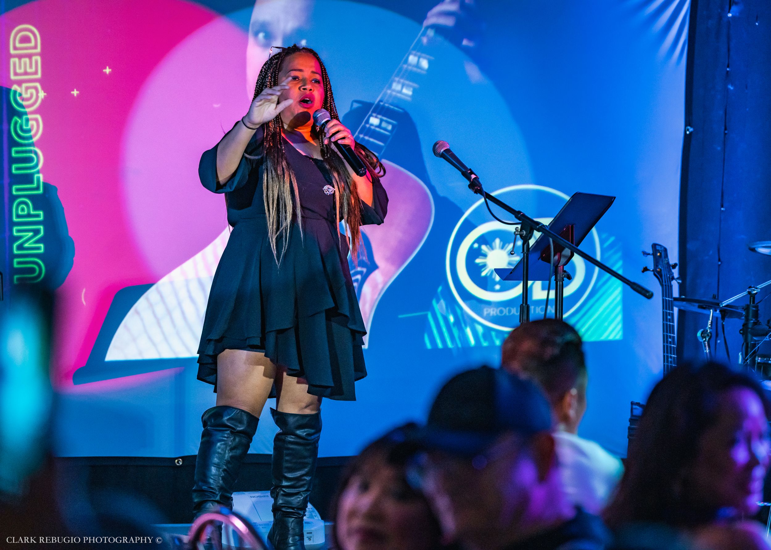 Female vocalist in black outfit performing on stage with colorful lights during a live music show.