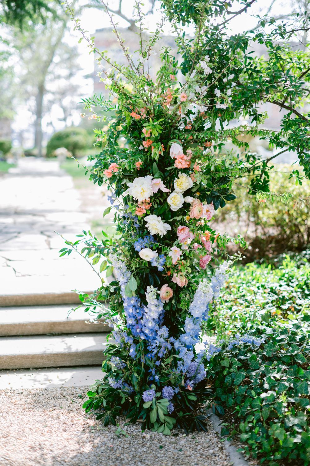 A sequence of delicate floral arrangements featuring pink roses and blue delphiniums against stone steps in a garden setting.