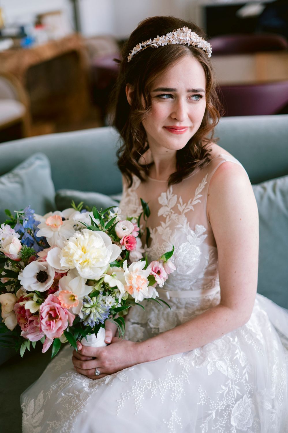 A bride in a detailed lace wedding gown holds a colorful bouquet featuring pink and white flowers.