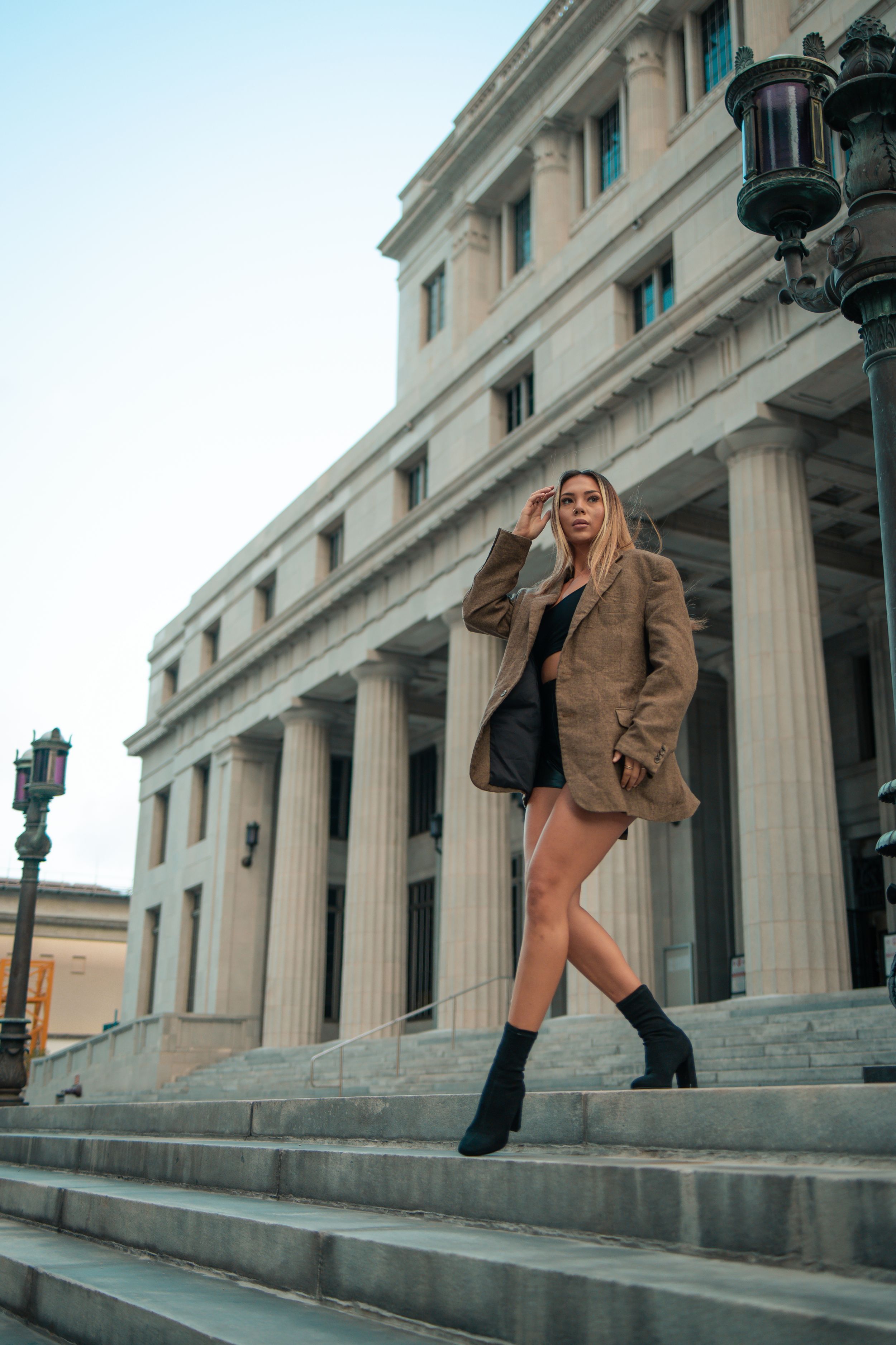 Model mid-step in brown jacket near courthouse columns, Fort Lauderdale fashion editorial portrait by Mannyportraits.