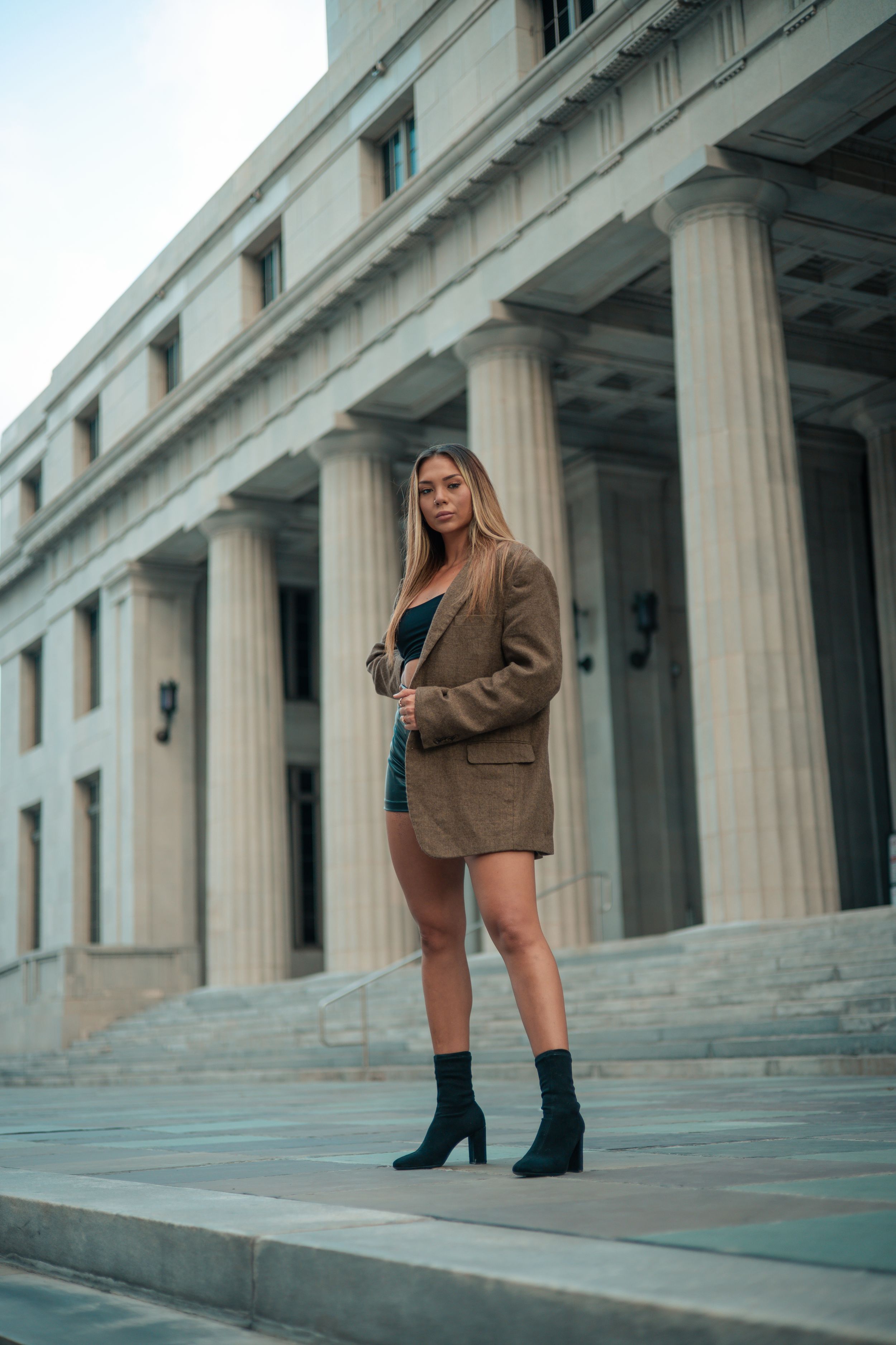 Model posing in brown coat by courthouse columns, West Palm Beach fashion editorial style, cinematic Mannyportraits shoot.