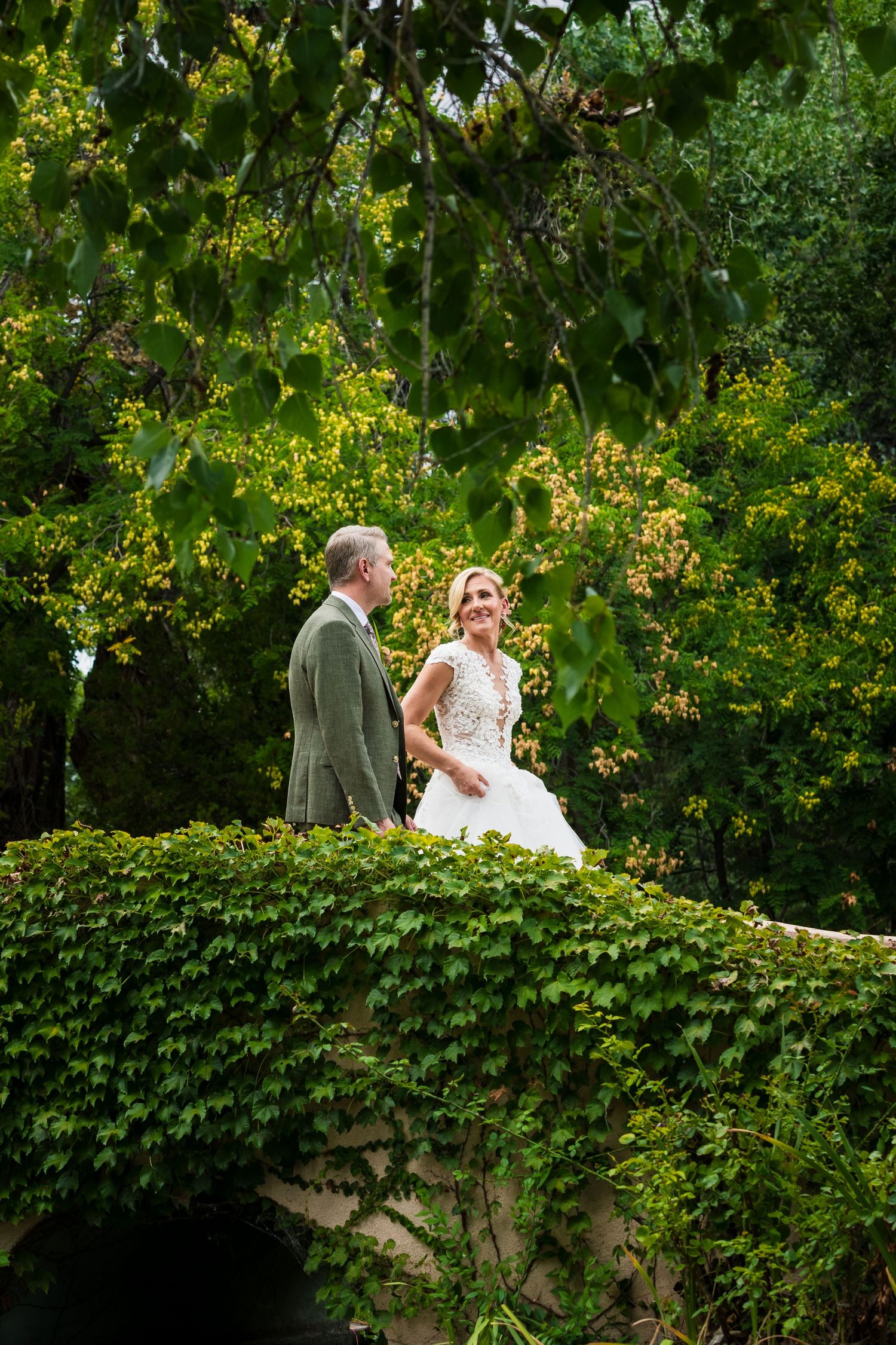 A couple shares a romantic moment on a lush garden wall covered in green ivy during a wedding photoshoot.