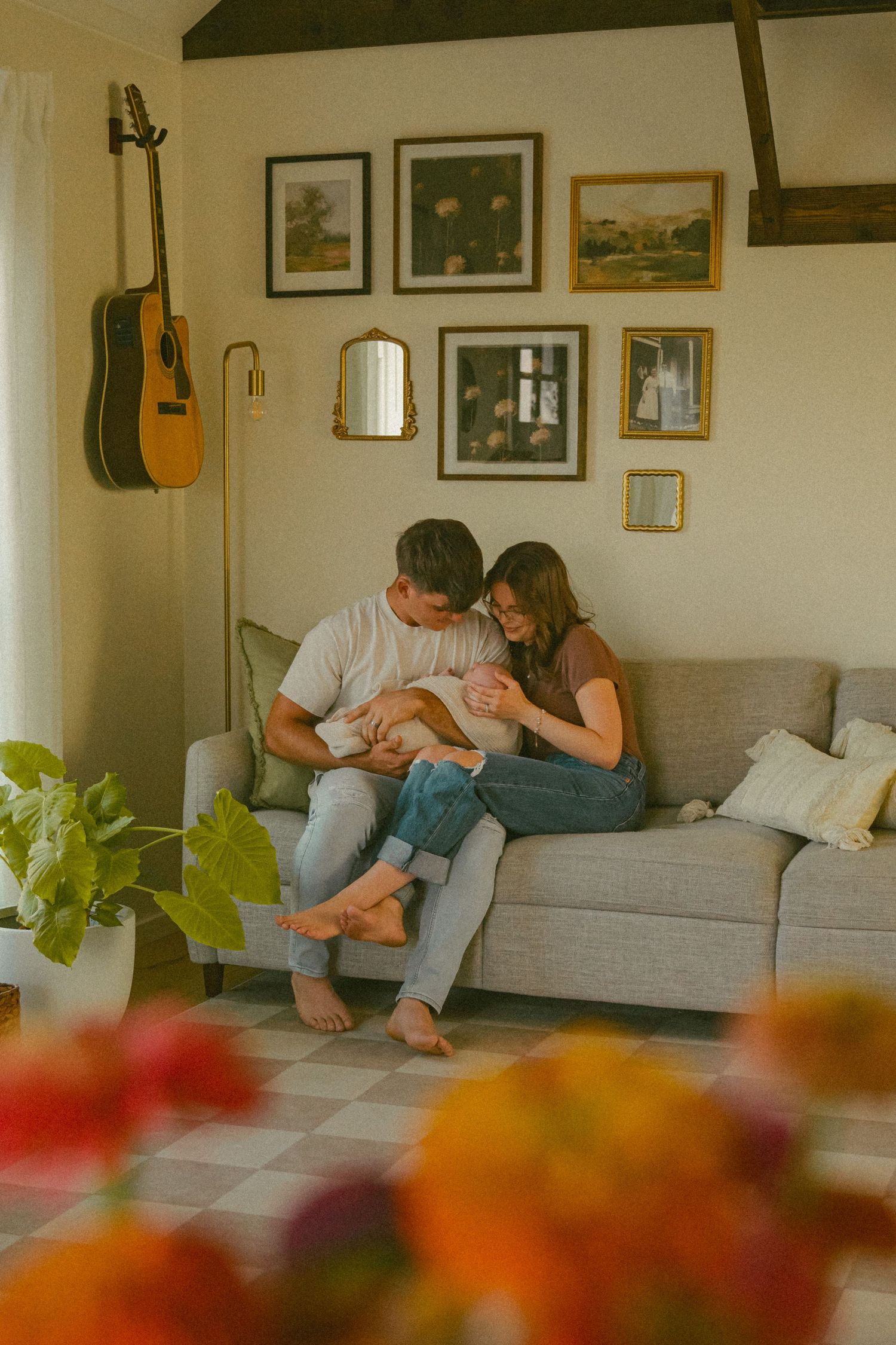 Intimate family moment on grey couch with guitar and artwork displayed on wall.