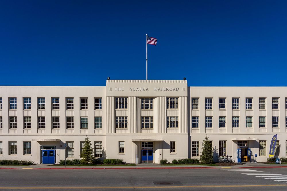 Four connected wide-angle exterior views of a historic white United States Post Office building under bright blue skies.