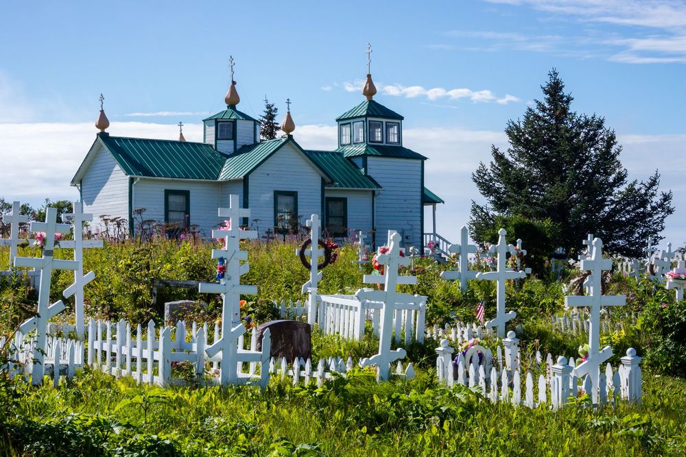 Historic lighthouse with white picket fence stands against blue sky and green foliage in Sequim, Washington.