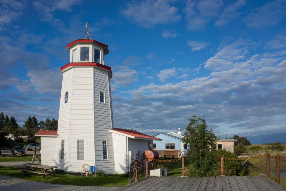 A line of small white lighthouses along a coastal shoreline with blue skies and puffy clouds overhead.