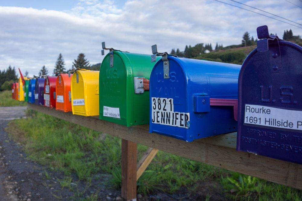 Colorful rural mailboxes line up along a country road with blue sky and green grass in the background.